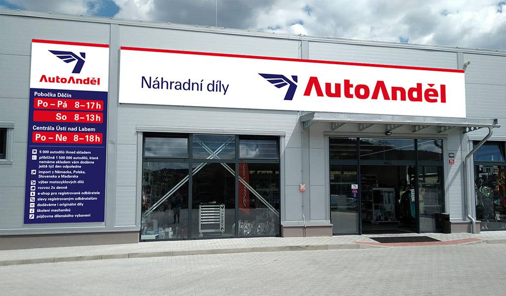 Obrázek zobrazuje průčelí nové prodejny Auto Anděl náhradní díly v Děčíně v barvách červené, modré a bílé. Nápis "Auto Anděl náhradní díly" se nachází nad vchodem do prodejny.